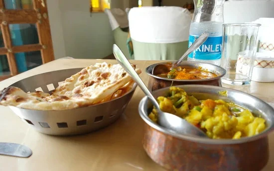 Indiase maaltijd met naanbrood, groentecurry en een fles water op een gedekte tafel.