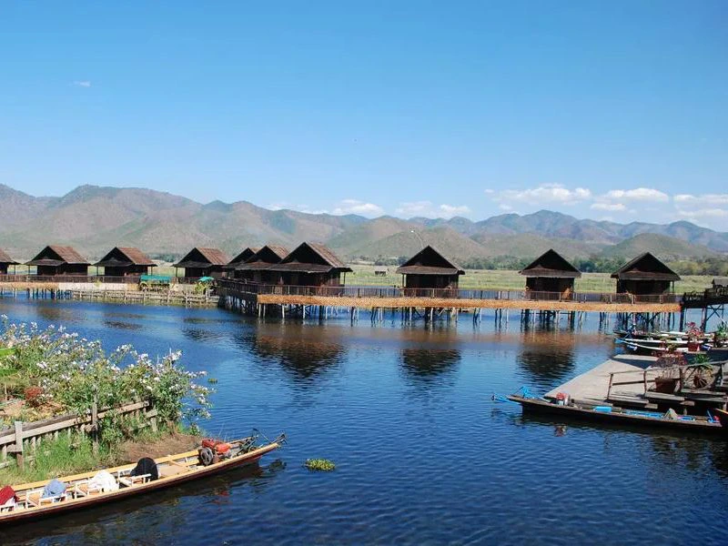Uitgestrekt wit zandstrand met helderblauwe zee en enkele mensen die genieten van de zon, onder een strakblauwe lucht.