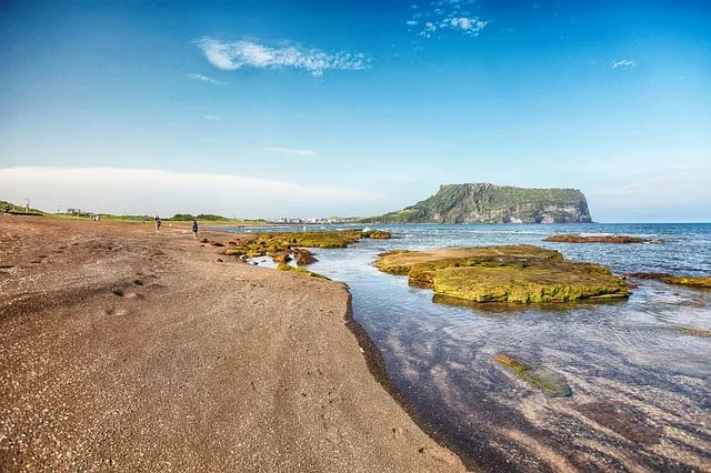 Strand met rotsplateaus langs de kust en een groene vulkanische krater in de verte op Jeju-eiland, Zuid-Korea.
