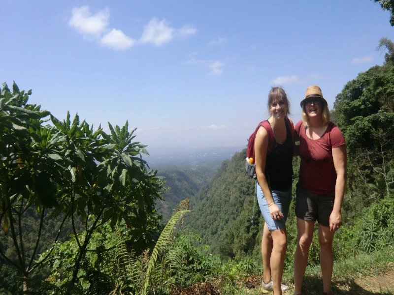 Twee vrouwen tijdens een wandeling in een groen, heuvelachtig landschap met uitzicht op een vallei in de verte.