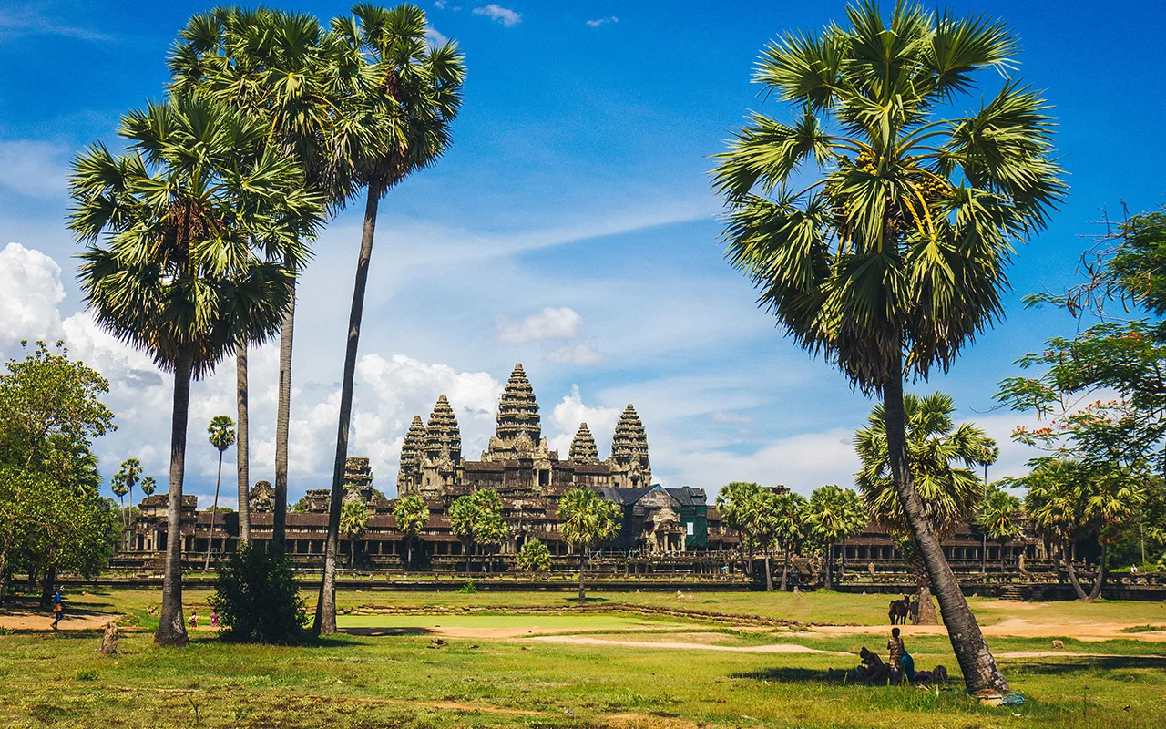 Uitzicht op de beroemde tempel Angkor Wat in Cambodja, omringd door palmbomen en een helderblauwe lucht.
