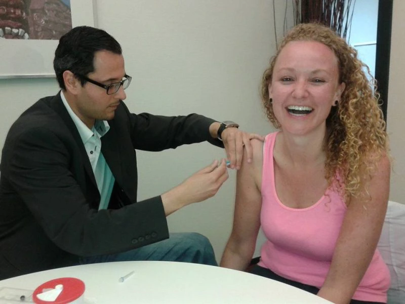 Vrouw lacht terwijl ze een vaccinatie krijgt van een arts in een kliniek.