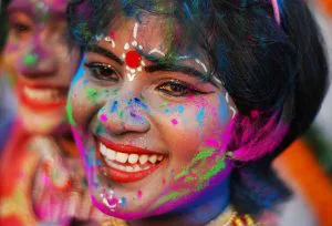 Vrouw met vrolijke glimlach heeft haar gezicht bedekt met felgekleurde poeders tijdens het Holi-festival.