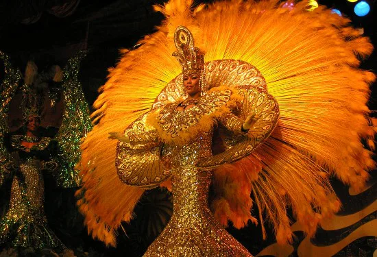 Danseres in gouden kostuum met grote veren waaier treedt op tijdens een kleurrijke show.