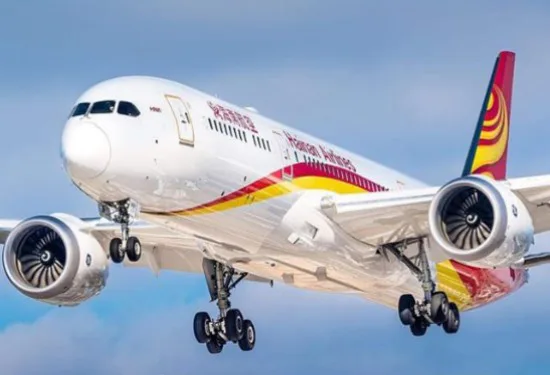Vliegtuig van Hainan Airlines in de lucht met uitgestoken landingsgestel, voorzien van een rood-geel kleurenschema en logo op de staart.