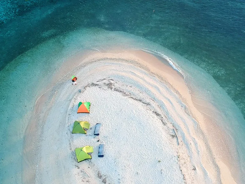 Luchtfoto van een klein zandstrand in zee met drie gekleurde tenten en enkele ligbedden.