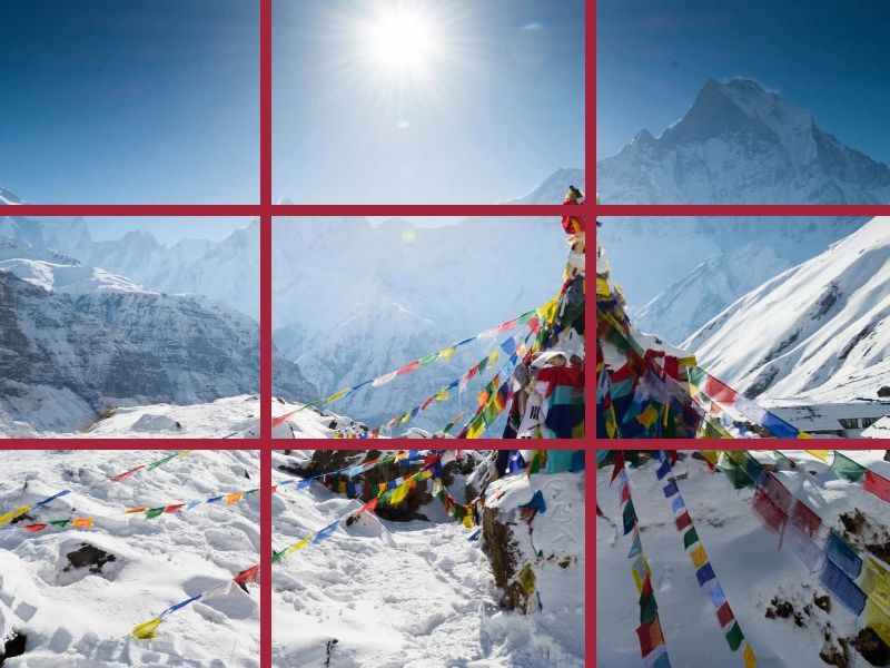 Kleurrijke gebedsvlaggen wapperen in een besneeuwd Himalaya-landschap met hoge bergen en felle zon.