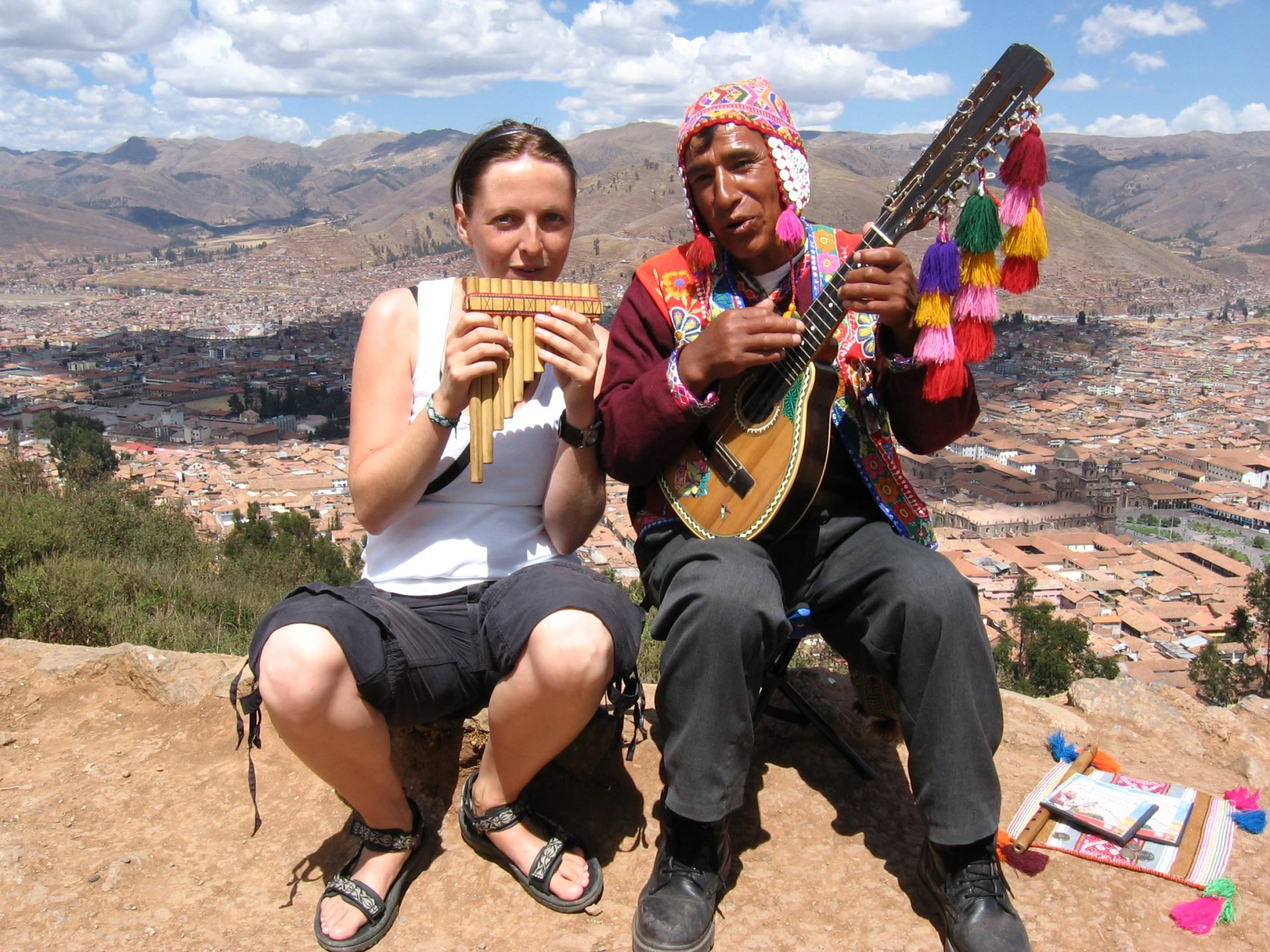 Reiziger en lokale muzikant spelen samen traditionele muziek met uitzicht op de stad Cusco in Peru.