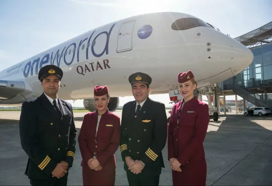 Twee piloten en twee stewardessen van Qatar Airways poseren voor een vliegtuig met het logo van oneworld op het vliegveld.