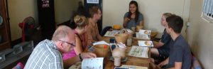Een groep mensen zit rond een houten tafel tijdens een kookworkshop, met menu’s en ingrediënten voor zich