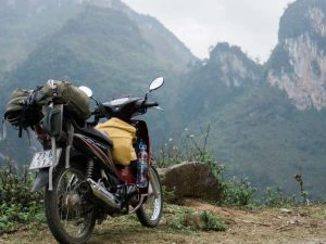 Motorfiets bepakt met tassen en bagage, geparkeerd aan de rand van een bergachtig landschap met mistige toppen.