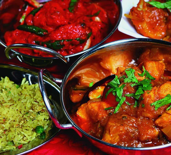 Indiaas diner met kleurrijke curry’s, rijst en gekruide groentegerechten in traditionele metalen schaaltjes.