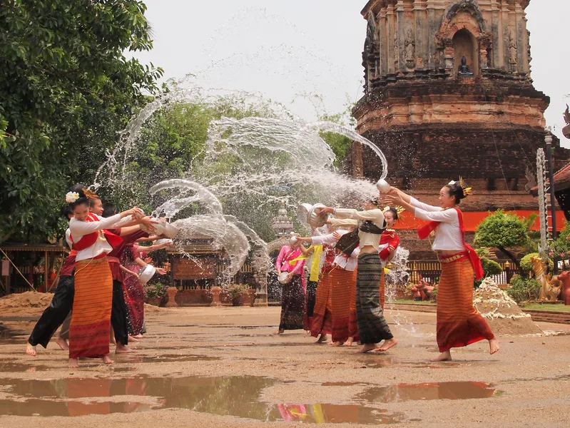 Vrouwen in traditionele kleding gooien water naar elkaar tijdens een feest bij een tempel.