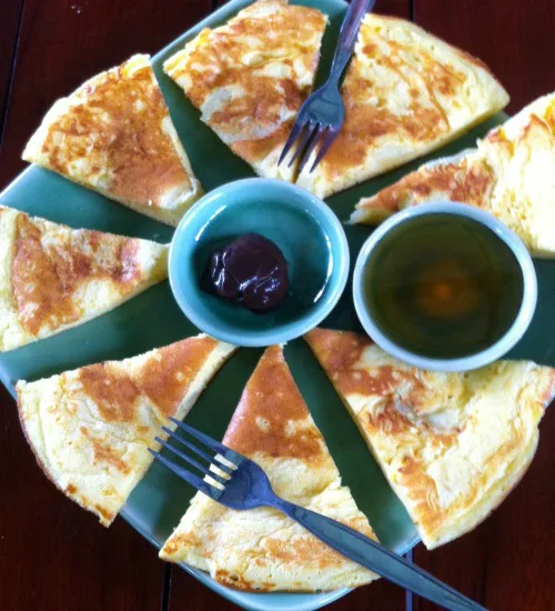 Bord met stukken pannenkoek, gerangschikt in een cirkel, met in het midden twee kommetjes gevuld met jam en thee.