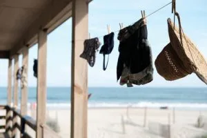 Lijn met wasknijpers waaraan kleding en een strohoed hangen te drogen, met op de achtergrond een zandstrand en zee.
