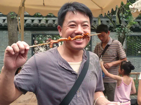 Man die lachend een spies met gegrild eten omhooghoudt op een lokale markt in China