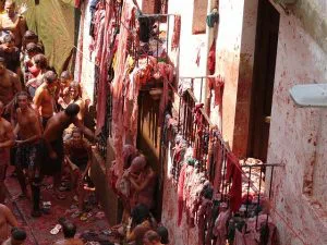 Mensen bedekt met tomatenpulp vieren het Tomatina-festival in een smalle straat met natte kleding aan de waslijnen.