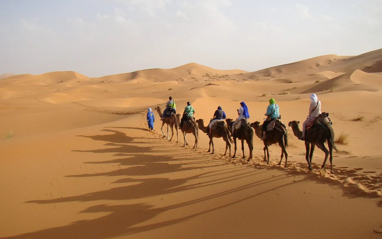 Rij mensen in kleurrijke kleding rijdt op kamelen door de zandduinen van de woestijn.