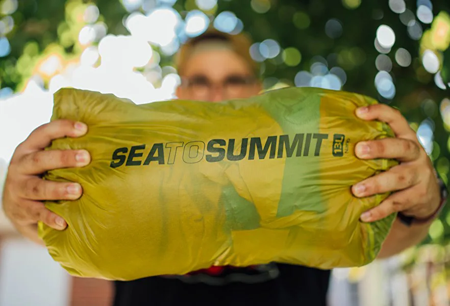 Zeven Sea to Summit waterdichte drybags in verschillende maten en kleuren, staand in oplopende volgorde van klein naar groot.