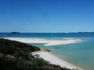 Uitzicht op een tropisch strand met wit zand, turquoise zee en een paar zeilboten aan de horizon bij de Whitsunday Islands, Australië.