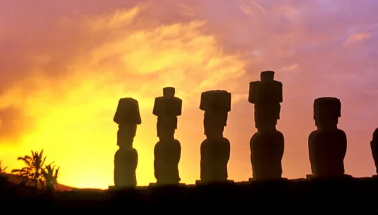 Silhouetten van Moai-beelden op Paaseiland tegen een kleurrijke zonsondergang.