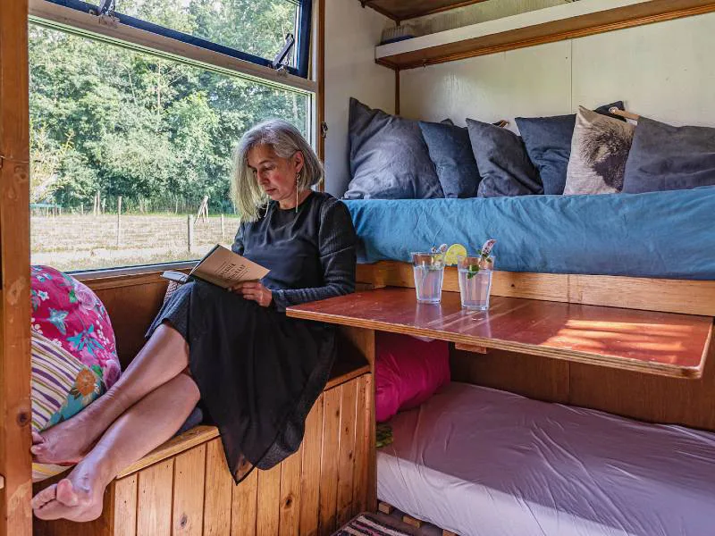Vrouw leest een boek in een knusse tiny house met uitzicht op een groen weiland