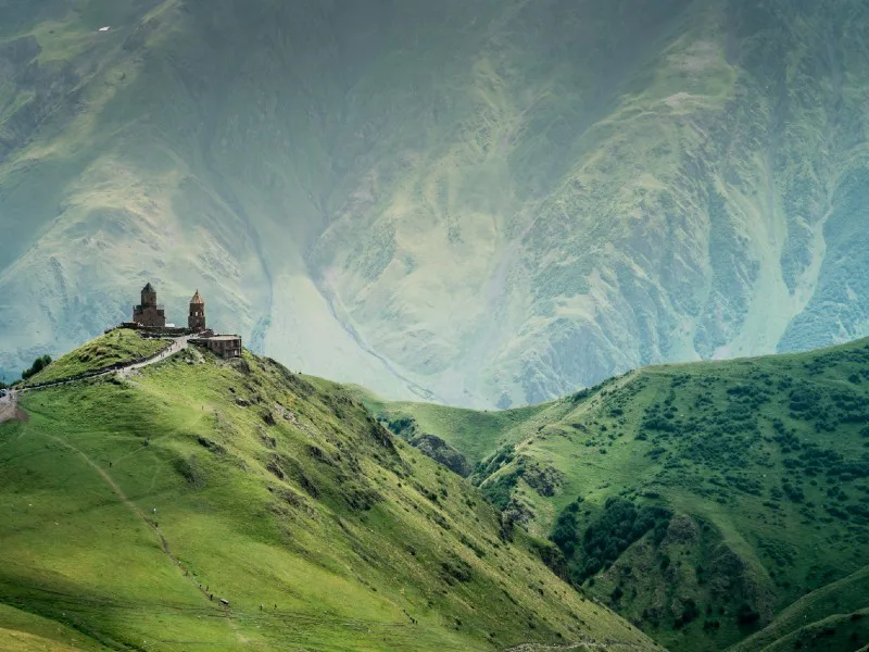 Kerk op een groene bergtop met hoge bergwanden op de achtergrond in Georgië.