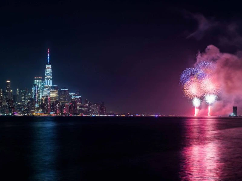 Vuurwerk boven het water met de verlichte skyline van een stad op de achtergrond tijdens de nacht.