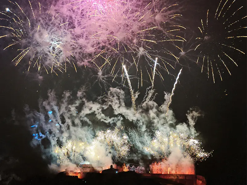 Vuurwerk boven een verlicht kasteel in de nacht, met kleurrijke vonken en rook die de lucht vullen.