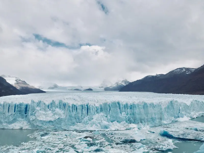 Grote gletsjer met grillige ijswand die uitloopt in een meer vol drijvende ijsschotsen, omringd door bergen.