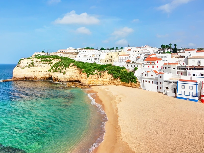 Breed zandstrand met turquoise zee en op de kliffen een dorp met witte huizen en rode daken in de Algarve, Portugal.
