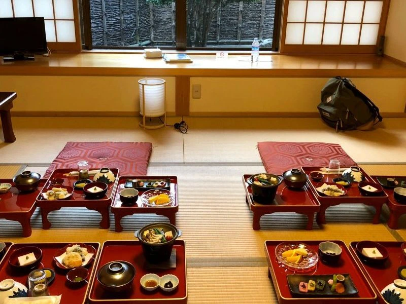 Traditionele Japanse maaltijd geserveerd op lage tafeltjes met zitkussens op tatamimatten, in een rustige ryokan-kamer met uitzicht op een tuin.