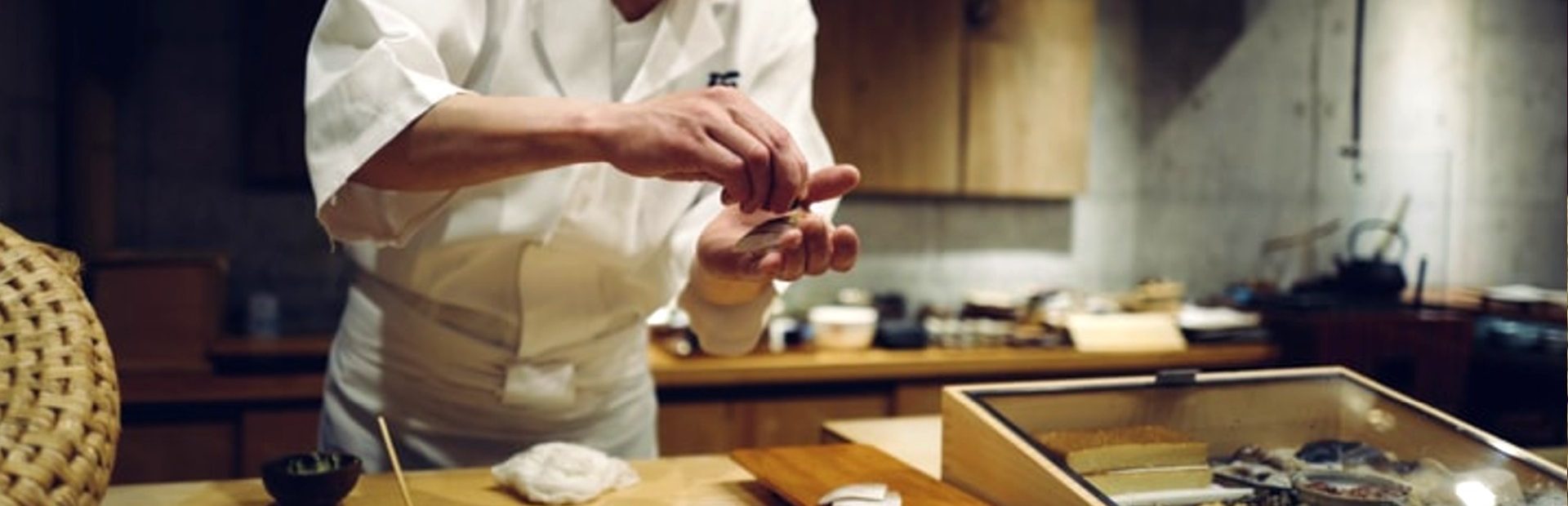 Sushichef in witte koksoutfit bereidt met zorg sushi achter de bar in een restaurant.