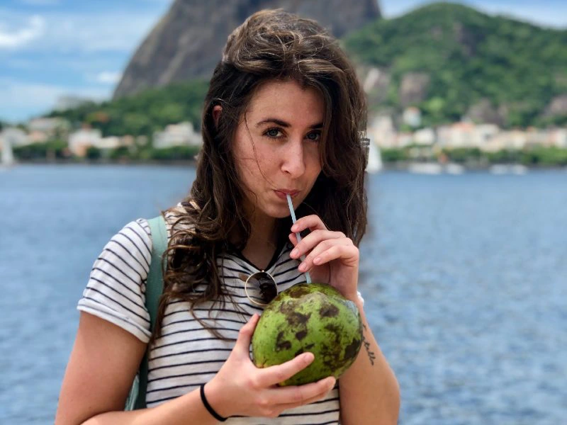 Vrouw drinkt uit een kokosnoot met een rietje aan het water, met op de achtergrond het iconische uitzicht van Rio de Janeiro