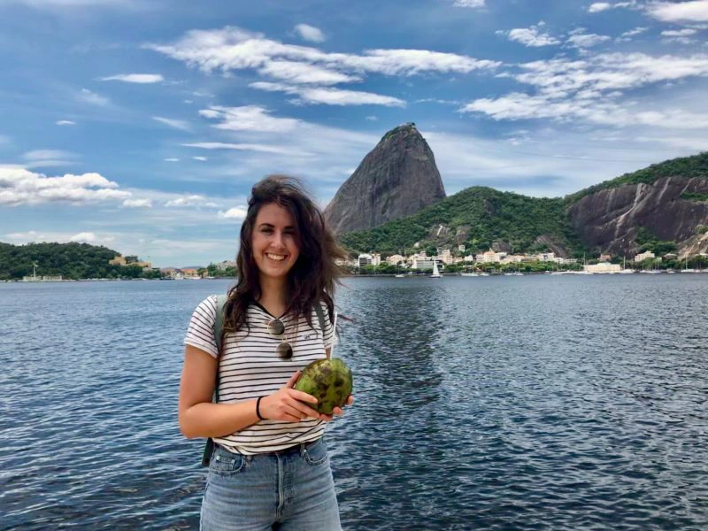 Vrouw met een kokosnoot in haar hand poseert aan het water met de Suikerbroodberg op de achtergrond in Rio de Janeiro, Brazilië.