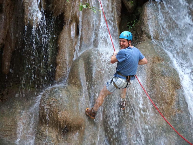 Man met klimgordel en helm abseilt langs een waterval over natte rotsen.