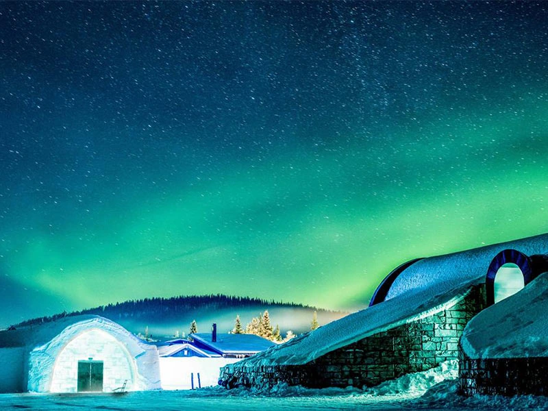 Een kleurrijke hemel vol noorderlicht boven een sneeuwwit landschap met iglo-achtige gebouwen in Lapland.