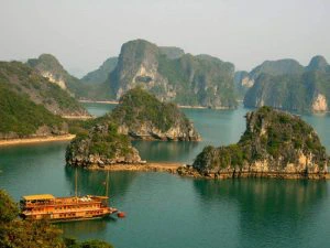 Traditionele houten boot vaart tussen groene kalkstenen eilanden in Halong Bay, Vietnam, omringd door kalm turquoise water.