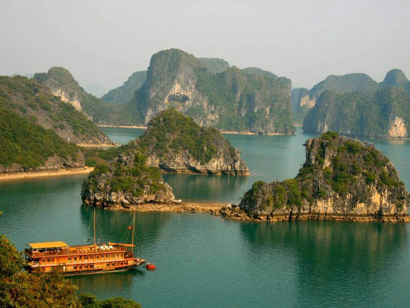 Traditionele houten boot vaart tussen groene kalkstenen eilanden in Halong Bay, Vietnam, omringd door kalm turquoise water.
