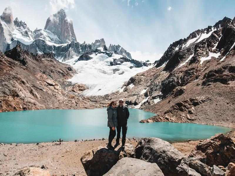 Twee reizigers bij El Chalten op een zonnige dag. Ze zijn de enige in beeld en staan bij het felblauwe meer.