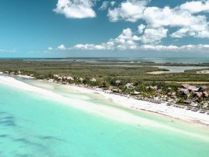 Luchtfoto van een tropisch strand met turquoise zeewater, wit zand en een rij hotels en palmbomen langs de kust.