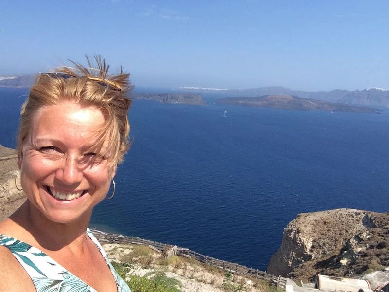 Vrouw maakt een selfie met op de achtergrond een helderblauwe zee en ruige kustlijn onder een stralend blauwe lucht.