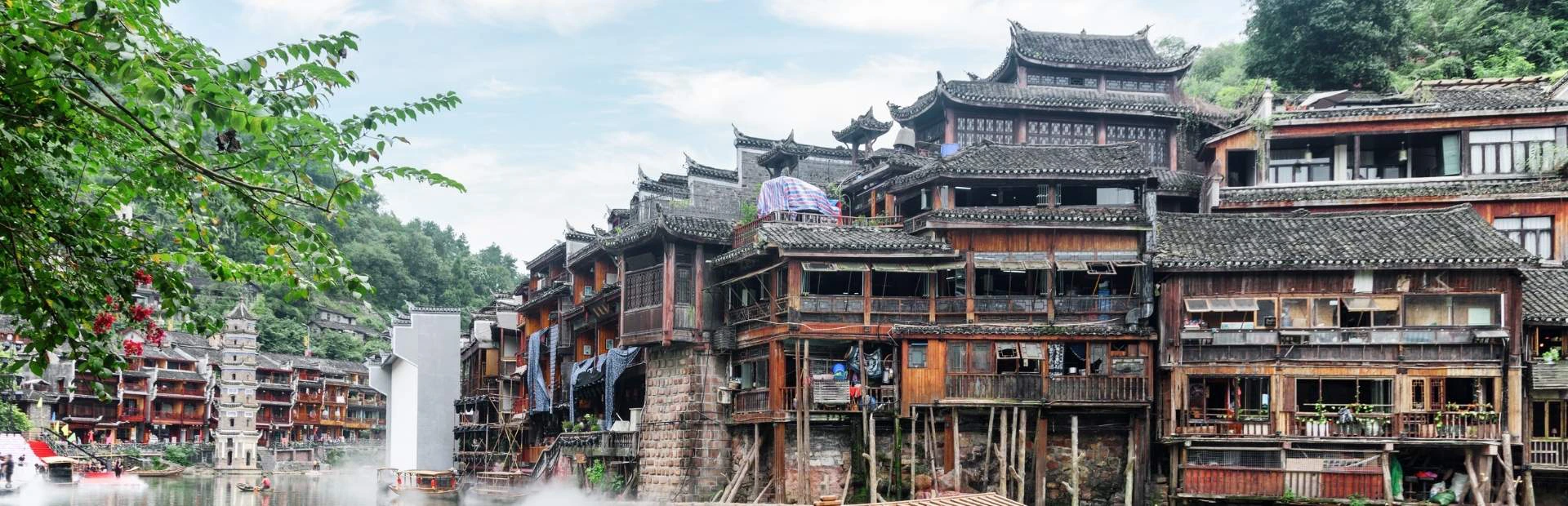 Traditionele houten huizen aan de rivier in het historische stadje Fenghuang, China, omgeven door groene heuvels en authentieke Chinese architectuur"