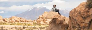 Reiziger zittend op een rots in het zuiden van Bolivia met op de achtergrond een berg met op de top sneeuw