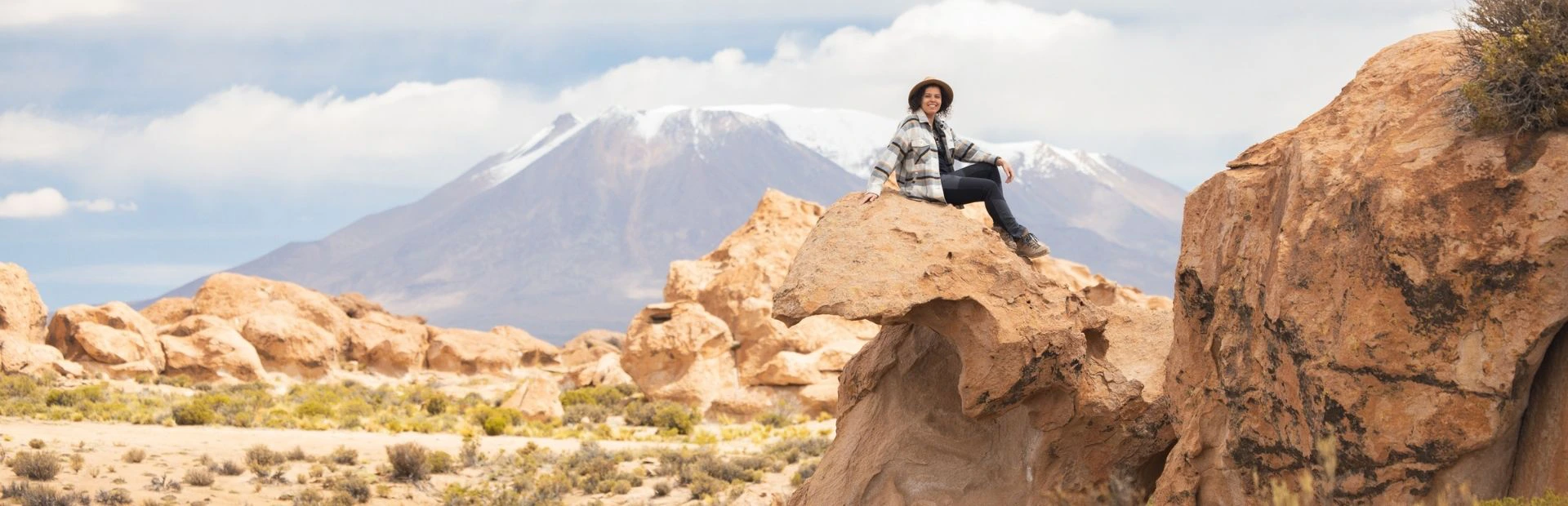 Reiziger zittend op een rots in het zuiden van Bolivia met op de achtergrond een berg met op de top sneeuw