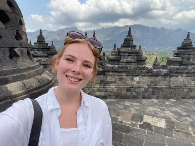 Vrouw maakt een selfie bij de Borobudur-tempel op Java, Indonesië, met stenen stoepa’s en bergen op de achtergrond.