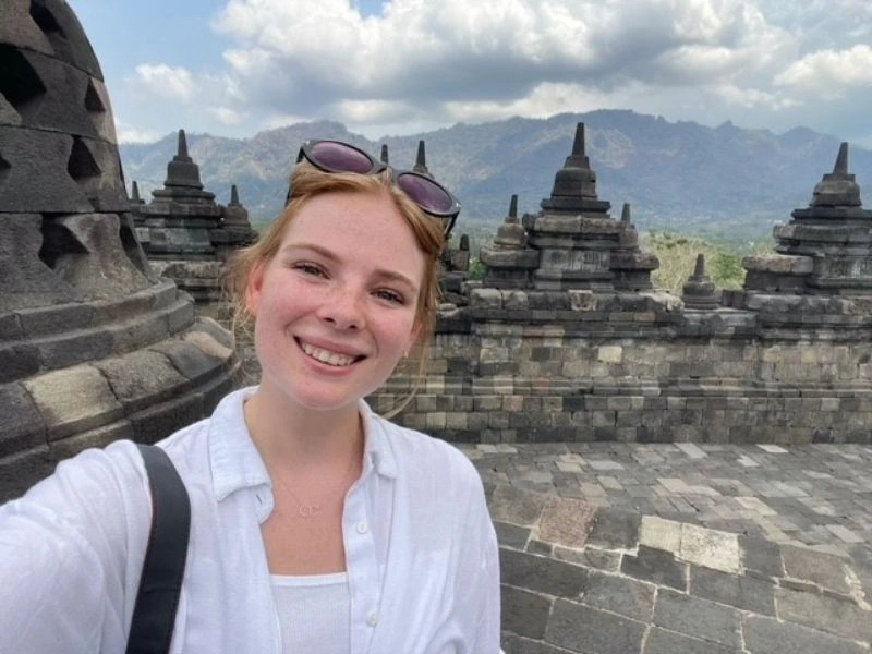 Vrouw maakt een selfie bij de Borobudur-tempel op Java, Indonesië, met stenen stoepa’s en bergen op de achtergrond.