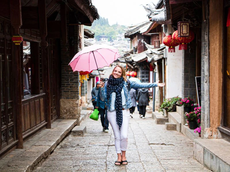Vrouw met roze paraplu loopt door een smalle straat met traditionele Chinese huizen en rode lantaarns