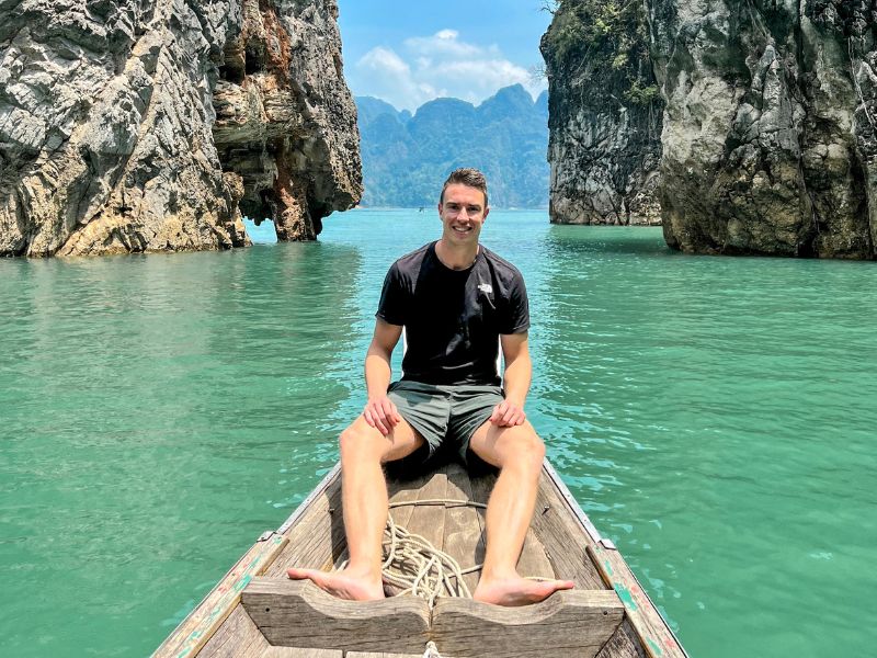 Man zit ontspannen op de punt van een houten boot, omringd door turquoise water en indrukwekkend kalksteenrotsen in Thailand
