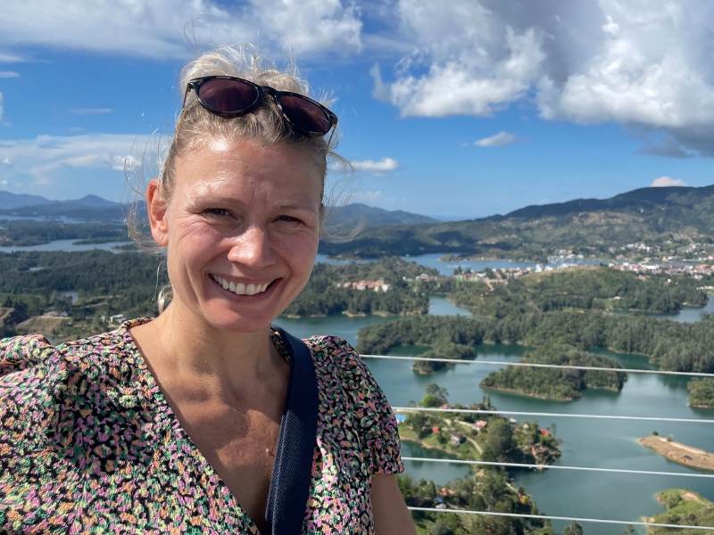 Lachende vrouw staat op een platform met huizen, bossen een meren op de achtergrond in Guatape.